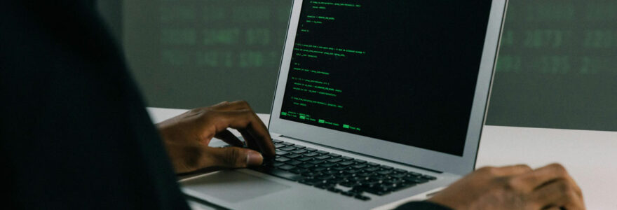 Développeur codant en Python sur un MacBook dans un bureau éclairé en vert.