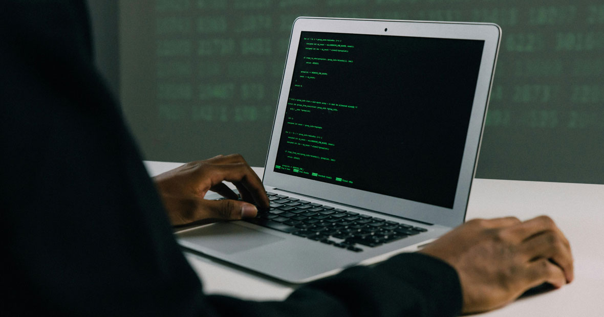 Développeur codant en Python sur un MacBook dans un bureau éclairé en vert.